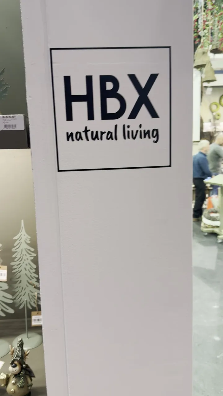 Kadr wypełnia biała kolumna z dużą czarną tabliczką HBX natural living. Po lewej stronie widoczna jest część półki z choinką i figurką renifera. Po prawej stronie kadru widać fragm